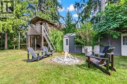 Expansive backyard featuring a stone fire pit, wood-built play structure, and two storage sheds - 