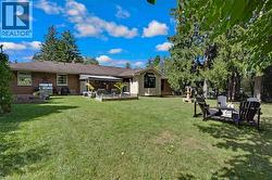 Expansive backyard featuring a manicured lawn, mature trees, a multi-tiered fountain, and a built-in outdoor patio with an awning - 