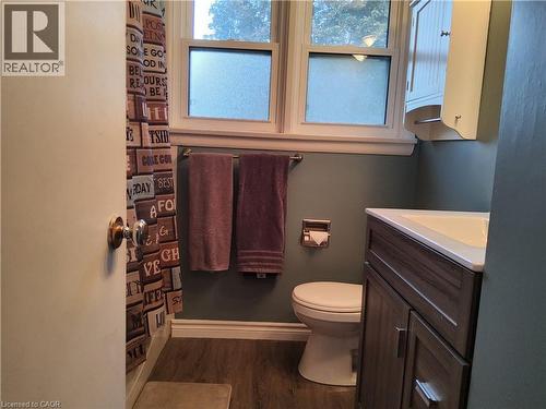 Wood-finish flooring, white vanity with integrated sink, wall-mounted cabinet, and frosted glass window - 33 Lee Avenue, Simcoe, ON 