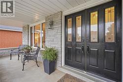 Double entry doors with decorative glass panels, stone facade, covered porch, and white framed windows - 