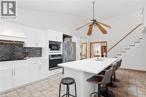 Kitchen featuring white cabinetry, dark tile backsplash, stainless steel appliances, and a central island with a white countertop - 76 Madeira Crescent, Cambridge, ON 