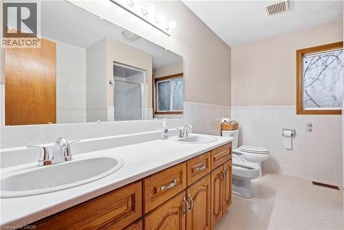 Dual vanity with chrome fixtures and integrated sinks, wood-finish cabinetry, full-width wall mirror, and white tiled wainscoting - 76 Madeira Crescent, Cambridge, ON 