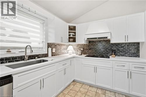 White shaker cabinetry, dark subway tile backsplash, white countertops, stainless steel sink with gooseneck faucet, and a built-in cooktop with range hood - 76 Madeira Crescent, Cambridge, ON 