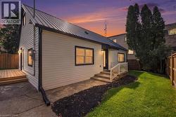 White horizontal siding exterior with a black metal roof, featuring a wooden deck, concrete patio, and fenced yard - 