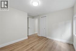 Light wood-finish flooring, white walls, flush mount ceiling light, white trim, and a white interior door - 