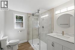 Contemporary bathroom featuring a glass-enclosed shower, single vanity with integrated sink, wood-finish flooring, and a circular mirror - 