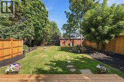 Expansive backyard featuring a manicured lawn, mature trees, wood privacy fencing, and a stone pathway - 