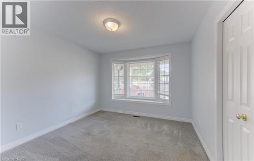 2nd Main Floor Bedroom featuring bay window with blinds, light gray wall paint, gray carpeting, white trim, and a ceiling-mounted light fixture and closet. - 25 Bankside Drive Unit# 2, Kitchener, ON 