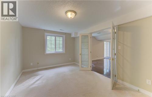 Carpeted room with a double-paned window, flush-mount ceiling light, and French doors featuring glass panels - 25 Bankside Drive Unit# 2, Kitchener, ON 