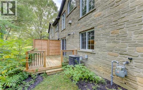 Stone exterior with multiple windows, leading to a wooden deck with dark balusters - 25 Bankside Drive Unit# 2, Kitchener, ON 