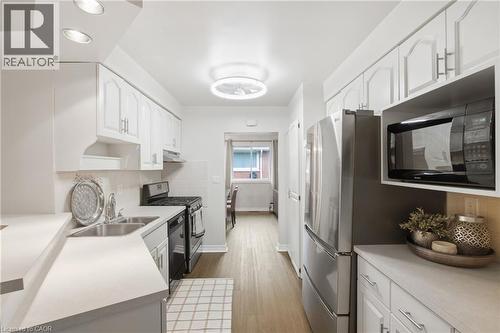 Galley kitchen with white cabinetry, stainless steel appliances, recessed lighting, and wood-finish flooring - 22 Sycamore Street, Hamilton, ON 