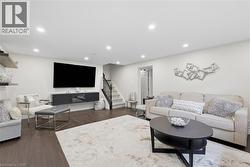 Recessed ceiling lighting, wood-finish flooring, staircase with dark wood railing, neutral wall color, and a built-in media console - 