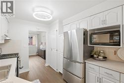 Kitchen featuring white cabinetry, stainless steel refrigerator, microwave, and wood-finish flooring - 