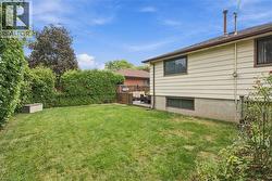 Expansive grass lawn bordered by mature hedges, featuring a wooden privacy fence and an elevated deck with wood flooring - 