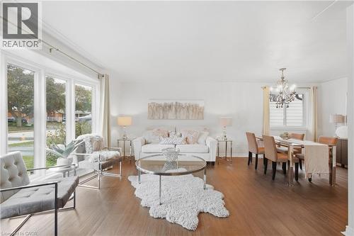 Expansive living and dining area featuring wood-finish flooring, a large bay window, and a chandelier light fixture - 22 Sycamore Street, Hamilton, ON 