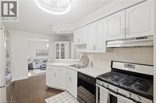 White kitchen cabinetry with stainless steel hardware, white countertops, built-in corner display cabinet, tile backsplash, and wood-finish flooring - 22 Sycamore Street, Hamilton, ON 