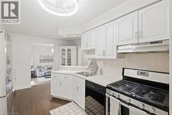 White kitchen cabinetry with stainless steel hardware, white countertops, built-in corner display cabinet, tile backsplash, and wood-finish flooring - 