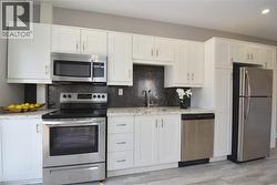 White shaker-style cabinetry with stainless steel hardware, stainless steel appliances, speckled stone countertops, and a dark textured backsplash - 