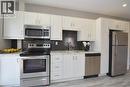 White shaker-style cabinetry with stainless steel hardware, stainless steel appliances, speckled stone countertops, and a dark textured backsplash - 76 Burlington Street E, Hamilton, ON 