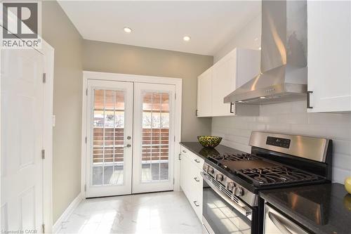 White cabinetry with black hardware, dark stone countertops, stainless steel appliances, white subway tile backsplash, and white French doors - 76 Burlington Street E, Hamilton, ON 