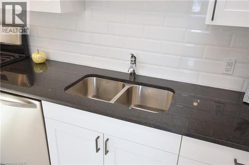 White shaker-style cabinetry with dark hardware, a dual-basin stainless steel sink, black speckled countertop, and white subway tile backsplash - 76 Burlington Street E, Hamilton, ON 