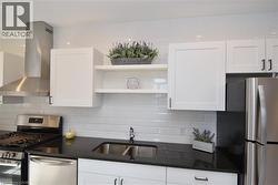 Modern kitchen featuring white shaker-style cabinetry, dark countertops, white subway tile backsplash, and stainless steel appliances - 