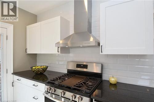 Kitchen featuring white shaker-style cabinetry, dark countertops, a subway tile backsplash, a stainless steel range, and a stainless steel hood vent - 76 Burlington Street E, Hamilton, ON 