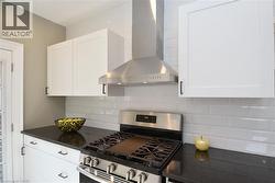 Kitchen featuring white shaker-style cabinetry, dark countertops, a subway tile backsplash, a stainless steel range, and a stainless steel hood vent - 