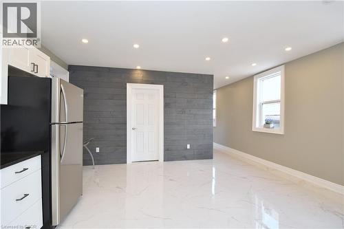 Recessed ceiling lighting illuminating white tile flooring, white cabinetry with black hardware, and a dark wood-paneled accent wall - 76 Burlington Street E, Hamilton, ON 