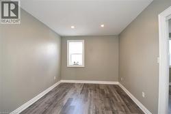 Recessed ceiling lighting, wood-finish flooring, neutral wall paint, white trim, and a single window - 