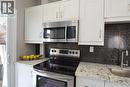 White shaker-style cabinetry, stainless steel microwave, black ceramic cooktop range, dark penny tile backsplash, and light-toned countertops - 76 Burlington Street E, Hamilton, ON 