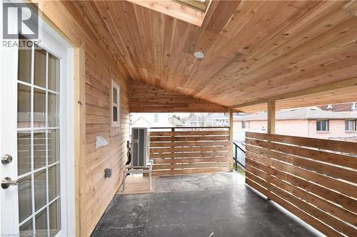 Covered outdoor patio featuring wood-finish ceiling, wood-finish siding, wood-slat privacy walls, and a glass-paneled exterior door - 76 Burlington Street E, Hamilton, ON 