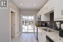 Kitchen featuring white cabinetry, light-toned countertops, a stainless steel sink, and wood-finish flooring - 