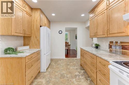 Wood-finish cabinetry with brass hardware, light-toned countertops, tile backsplash, recessed lighting, and a built-in refrigerator alcove - 422 Grangewood Drive, Waterloo, ON 