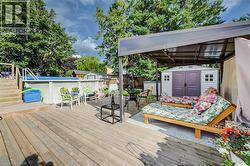 Expansive wood-finish deck featuring an above-ground pool with stairs, a covered patio area, and a storage shed - 
