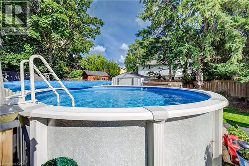Above-ground pool with integrated ladder, surrounded by mature trees and a privacy fence - 422 Grangewood Drive, Waterloo, ON 