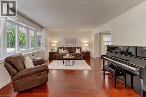Elegant living room showcasing gleaming wood-finish flooring, abundant natural light from multi-panel glass doors and windows, a grand piano, and warm ambient lighting from table lamps - 422 Grangewood Drive, Waterloo, ON 