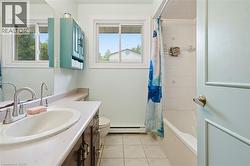 Bright, galley-style bathroom featuring dual vanity sinks with brushed nickel faucets, ceramic tile flooring, and a tile-lined shower enclosure with glass door - 
