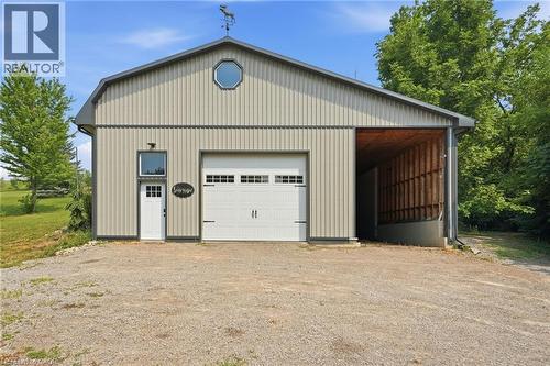 Barn-style structure featuring corrugated metal siding, a weather vane, a large garage door, an octagonal window, and an open covered area - 1311 W Concession 6 Road, Flamborough, ON 