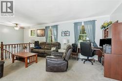 Carpeted living area with a built-in office desk, multiple windows, and a ceiling fan with integrated lighting - 
