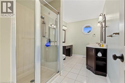 Glass-enclosed shower with a handheld showerhead, dark wood vanity with white countertop, octagonal window, and wall-mounted sconce lighting - 141 Race Street, Paris, ON 