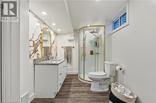 Bathroom featuring a dual-sink vanity with a granite-style countertop, a gold-framed arched mirror, a corner shower with gold-finish trim, and wood-finish flooring - 141 Race Street, Paris, ON 