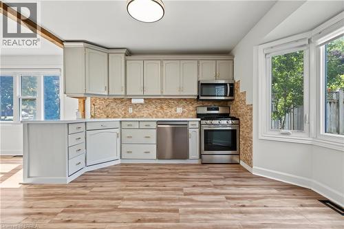 Light-toned cabinetry with stainless steel appliances, stone-finish backsplash, and wood-finish flooring - 141 Race Street, Paris, ON 