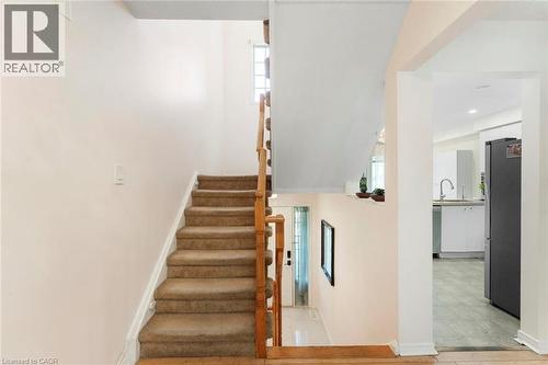 Carpeted staircase with wood-finish handrail, transom window, and an arched entry to a kitchen featuring white cabinetry and stainless-steel appliances - 123 Brickyard Way, Brampton, ON 