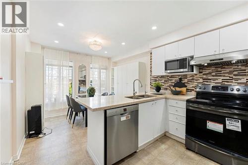 White cabinetry, stainless steel appliances, mosaic tile backsplash, recessed lighting, and a kitchen island with integrated sink - 123 Brickyard Way, Brampton, ON 
