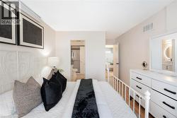 White metal bed frame, light wood-finish flooring, white dresser with black hardware, white walls, and a wall-mounted air conditioning unit - 