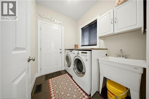 Functional utility room featuring dark tile flooring, white upper cabinetry, a window with blinds, and a built-in utility sink - 167 Broadoaks Drive, Cambridge, ON 