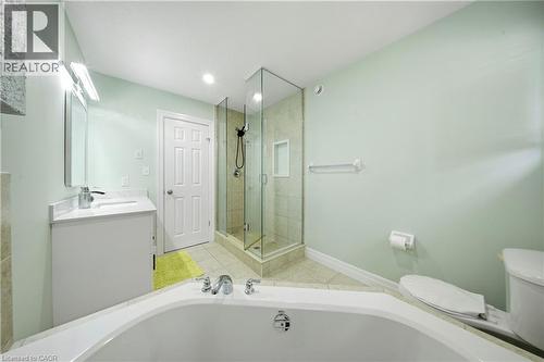 Corner soaking tub, glass-enclosed shower with tile surround, single vanity with integrated sink, tile flooring, and recessed lighting - 167 Broadoaks Drive, Cambridge, ON 
