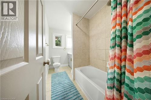 White paneled door with brass hardware, light-colored wall tile, white bathtub, and a window providing natural light - 167 Broadoaks Drive, Cambridge, ON 