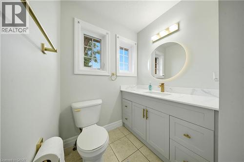 Light-toned floor tiling, dual windows, single vanity with light-toned cabinetry, light-toned countertop, and gold-finish fixtures - 167 Broadoaks Drive, Cambridge, ON 